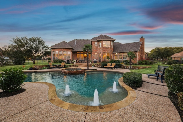 pool at dusk with a lawn, an in ground hot tub, pool water feature, and a patio