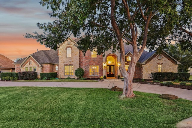 view of front of house featuring french doors, a lawn, brick siding, and driveway