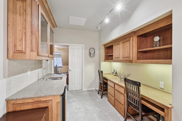 kitchen with backsplash, light stone counters, light colored carpet, sink, and built in desk