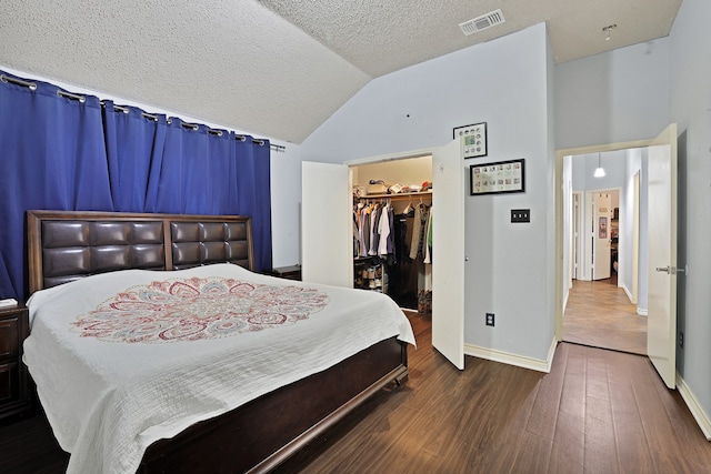 bedroom with high vaulted ceiling, hardwood / wood-style floors, a textured ceiling, a walk in closet, and a closet