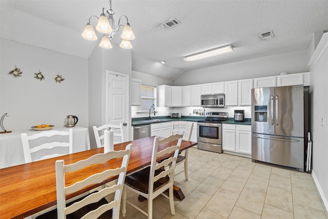 kitchen with white cabinetry, decorative light fixtures, stainless steel appliances, and vaulted ceiling