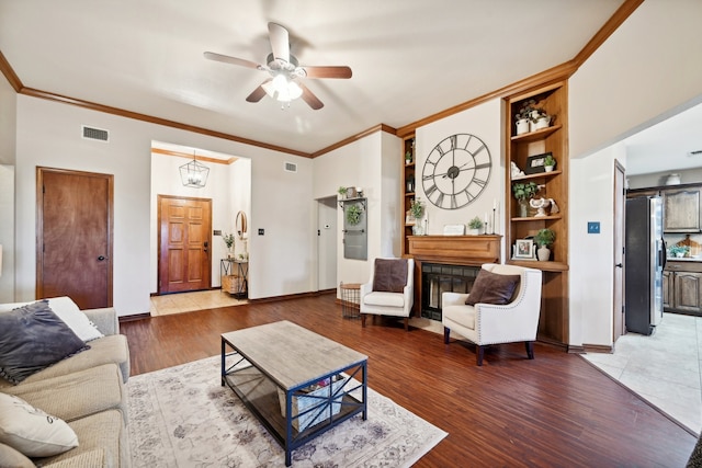 living room featuring built in shelves, ceiling fan, hardwood / wood-style floors, and crown molding