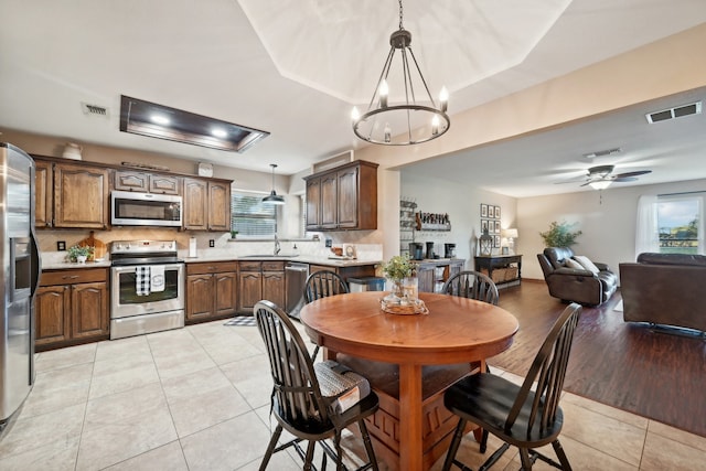 dining space with sink, light hardwood / wood-style floors, and ceiling fan with notable chandelier