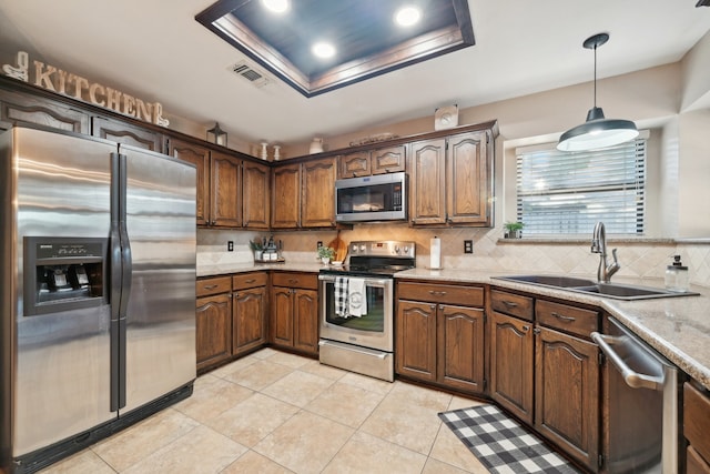 kitchen featuring decorative backsplash, appliances with stainless steel finishes, light stone countertops, sink, and decorative light fixtures