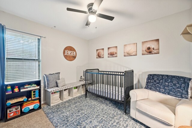 carpeted bedroom featuring ceiling fan and a crib