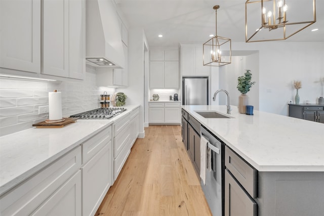 kitchen with custom range hood, decorative light fixtures, a center island with sink, and sink