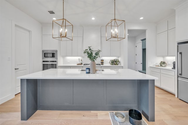 kitchen with a kitchen island with sink, light hardwood / wood-style flooring, hanging light fixtures, and appliances with stainless steel finishes