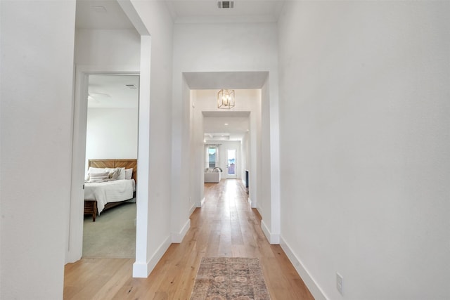 corridor with ornamental molding, light hardwood / wood-style floors, and a notable chandelier