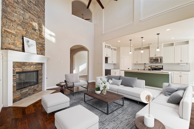 living room with a stone fireplace, sink, dark hardwood / wood-style floors, and a high ceiling