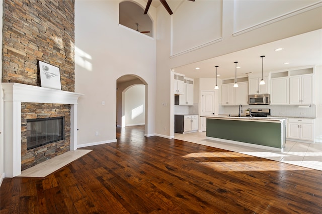 unfurnished living room with ceiling fan, sink, a stone fireplace, a towering ceiling, and light hardwood / wood-style floors