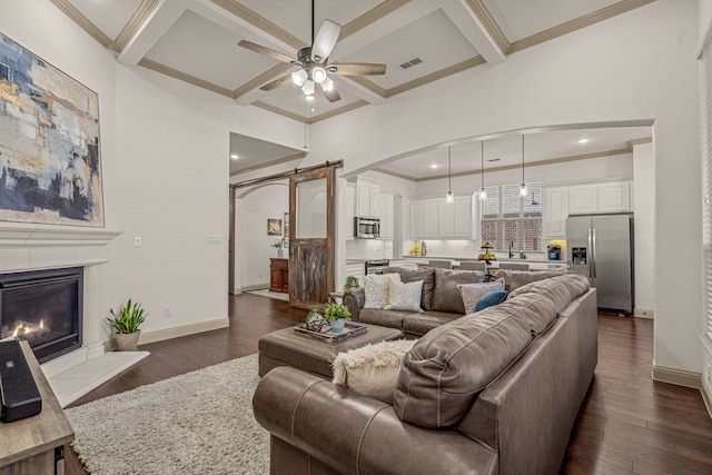 living room with a barn door, ceiling fan, dark wood-type flooring, and coffered ceiling