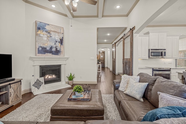 living room with a barn door, crown molding, ceiling fan, and dark hardwood / wood-style floors