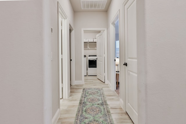 hall with independent washer and dryer and light wood-type flooring