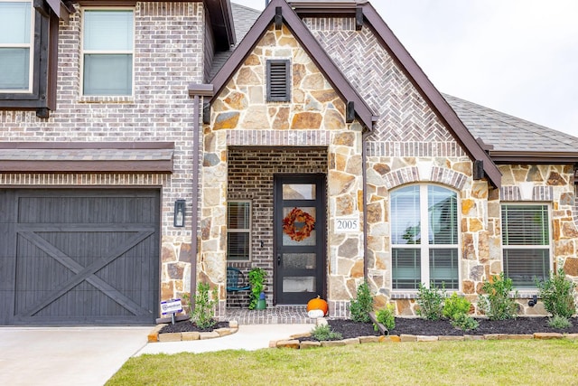 entrance to property featuring a garage, stone siding, brick siding, and driveway