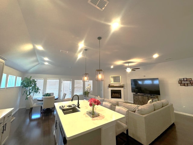 kitchen featuring sink, hanging light fixtures, white cabinets, a center island with sink, and vaulted ceiling