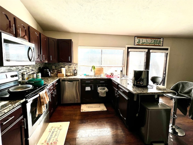 kitchen with dark hardwood / wood-style flooring, backsplash, stainless steel appliances, sink, and stone counters