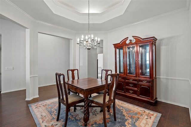 dining space with an inviting chandelier, crown molding, a tray ceiling, and dark wood-type flooring