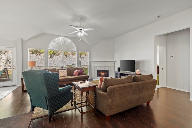 living room with dark hardwood / wood-style floors, vaulted ceiling, ceiling fan, and a tiled fireplace