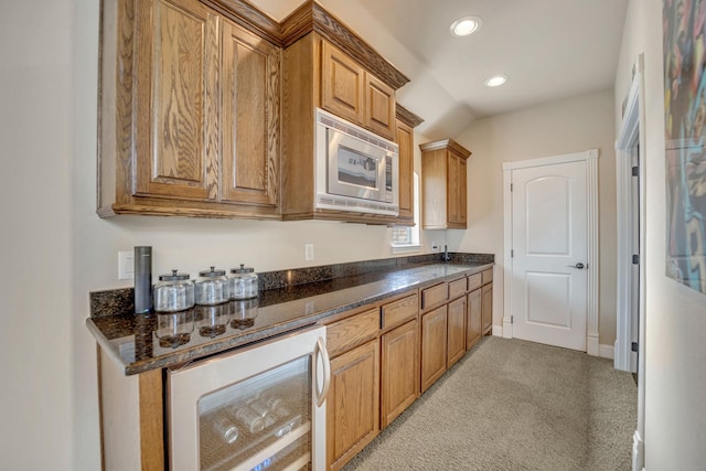 bar featuring stainless steel microwave, dark stone counters, beverage cooler, and light carpet