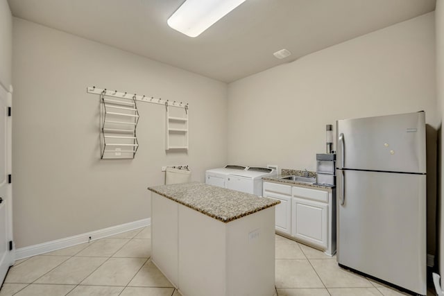 kitchen with white cabinetry, sink, stainless steel fridge, light tile patterned floors, and independent washer and dryer