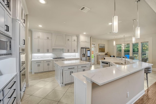 kitchen featuring custom exhaust hood, white cabinetry, hanging light fixtures, appliances with stainless steel finishes, and a large island