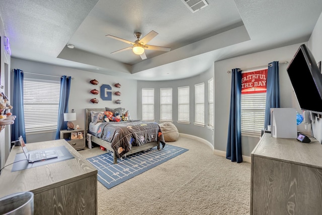 bedroom featuring light carpet, ceiling fan, a tray ceiling, and a textured ceiling