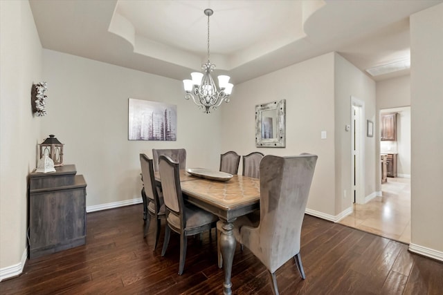 dining room with an inviting chandelier, a tray ceiling, and dark wood-type flooring