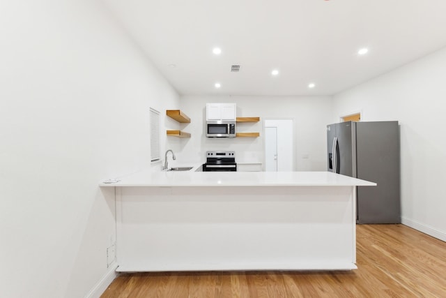 kitchen with kitchen peninsula, sink, appliances with stainless steel finishes, light hardwood / wood-style floors, and white cabinetry