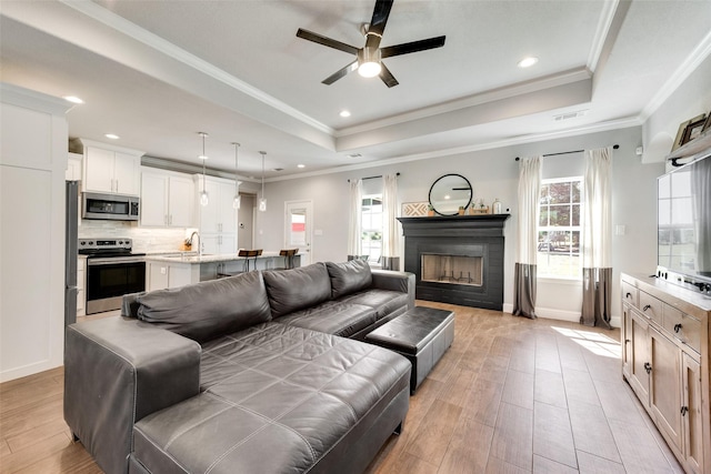 living room featuring a tray ceiling, plenty of natural light, ornamental molding, and sink