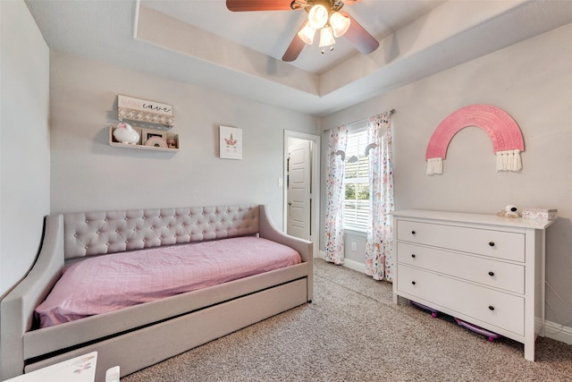 carpeted bedroom with a raised ceiling and ceiling fan