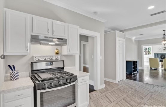 kitchen with white cabinets, crown molding, light wood-type flooring, decorative light fixtures, and gas stove