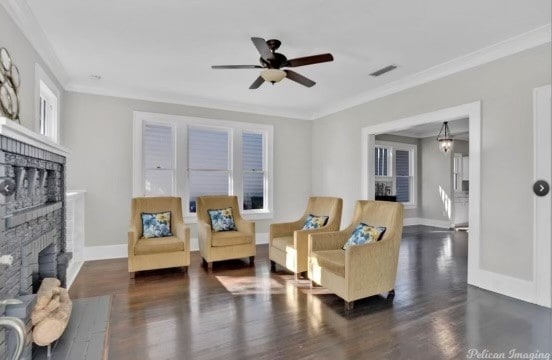 living room featuring ceiling fan with notable chandelier, dark hardwood / wood-style flooring, a brick fireplace, and ornamental molding