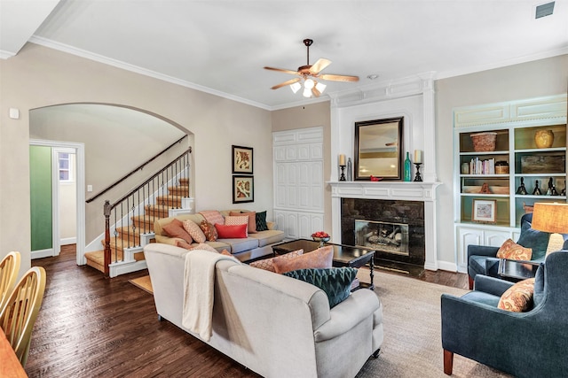 living room with a high end fireplace, ornamental molding, ceiling fan, and dark wood-type flooring