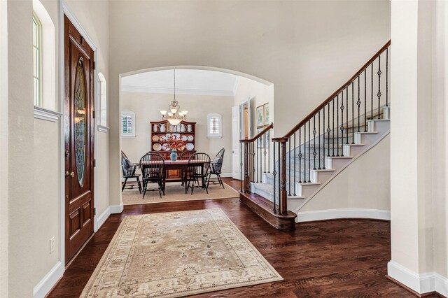 entryway with dark hardwood / wood-style floors, plenty of natural light, crown molding, and a chandelier