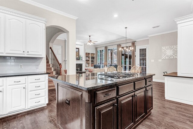 kitchen with white cabinetry, dark hardwood / wood-style floors, dark stone countertops, stainless steel gas stovetop, and ornamental molding