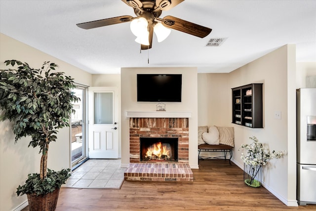 living room with a fireplace, ceiling fan, light hardwood / wood-style flooring, and a textured ceiling