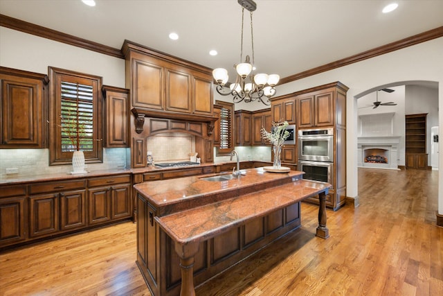 kitchen with stone counters, arched walkways, a center island with sink, appliances with stainless steel finishes, and a sink