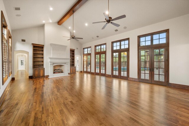 unfurnished living room featuring french doors, visible vents, a fireplace with raised hearth, wood finished floors, and beamed ceiling