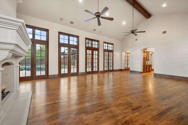 unfurnished living room featuring arched walkways, wood finished floors, visible vents, baseboards, and beam ceiling