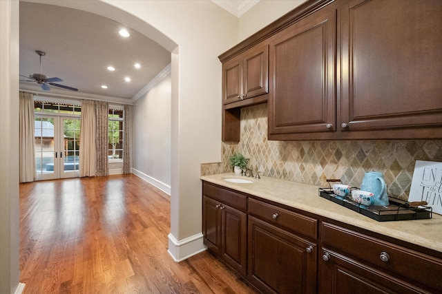 kitchen featuring tasteful backsplash, arched walkways, crown molding, light wood-type flooring, and a sink