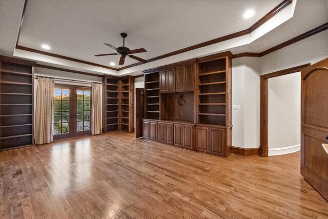 unfurnished living room featuring light wood-type flooring, ornamental molding, a raised ceiling, and french doors