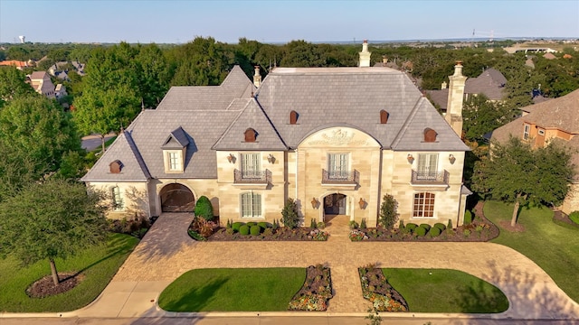 french country home with a chimney, a balcony, and a front lawn