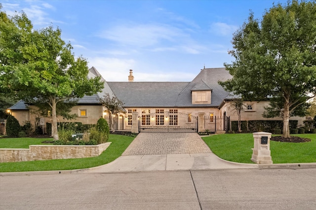 french country home with a fenced front yard, a gate, a chimney, and a front yard