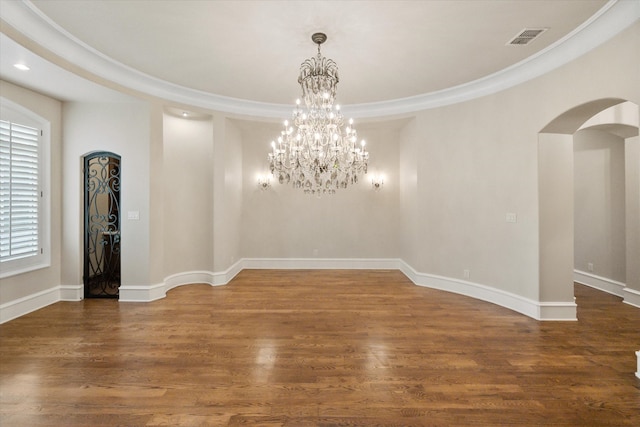 unfurnished room with arched walkways, wood finished floors, visible vents, and baseboards