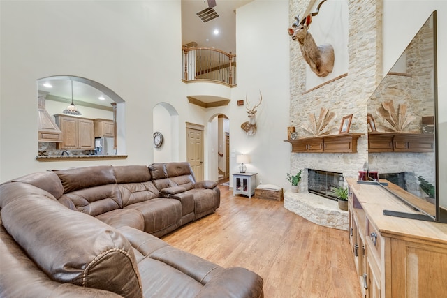 living room with light wood-type flooring, a fireplace, and a high ceiling