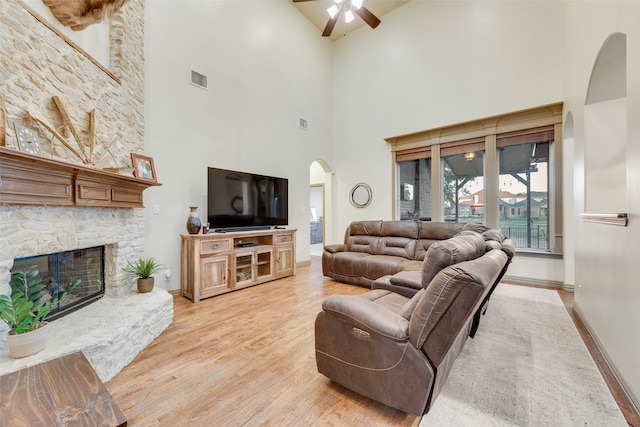 living room featuring light wood-type flooring, a fireplace, a towering ceiling, and ceiling fan