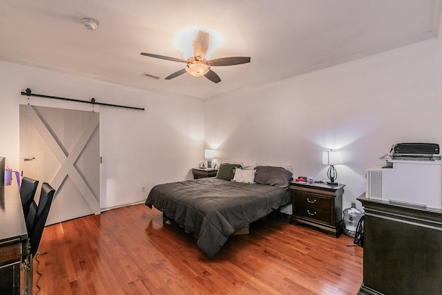 bedroom with hardwood / wood-style floors, a barn door, ceiling fan, and crown molding