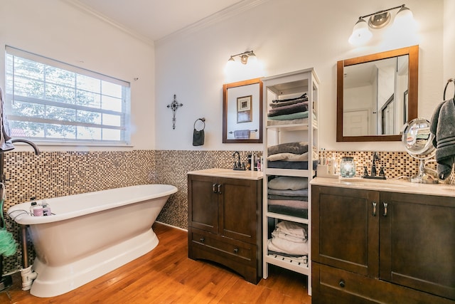 bathroom featuring hardwood / wood-style floors, vanity, ornamental molding, a tub to relax in, and tile walls