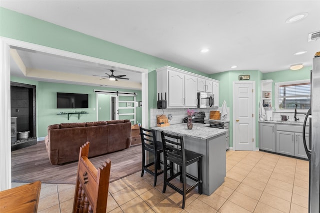 kitchen with a kitchen bar, appliances with stainless steel finishes, light wood-type flooring, a barn door, and white cabinetry