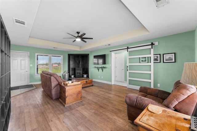 living room with a tray ceiling, a barn door, ceiling fan, and hardwood / wood-style flooring